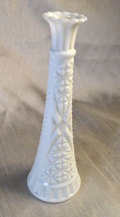 a small white vase sitting on top of a wooden table next to a gray wall