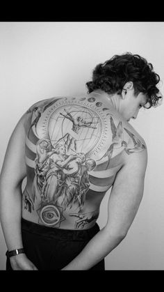 a man with tattoos on his back standing in front of a wall