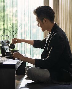 a young man sitting on the floor pouring tea into a cup with a teapot in front of him