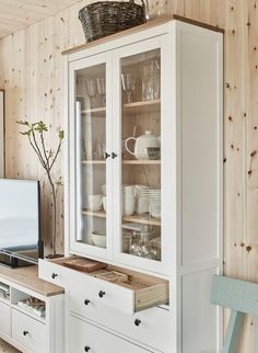 a white china cabinet with glass doors and drawers in a wood paneled living room