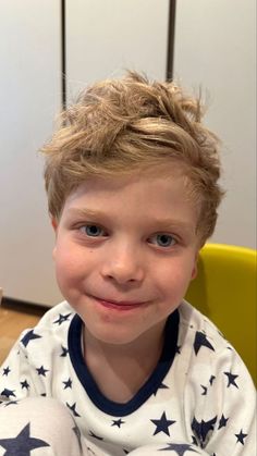 a young boy with blonde hair wearing pajamas and smiling at the camera while sitting in a chair