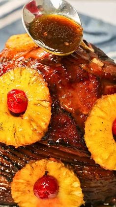 a plate topped with pineapples and meat covered in syrup next to a spoon