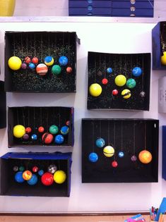 several black boxes with different colored balls in them on a white wall next to pens and pencils