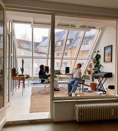 two people are sitting in an open room with large windows and plants on the floor