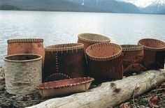 several baskets sitting on top of a log next to the water with mountains in the background