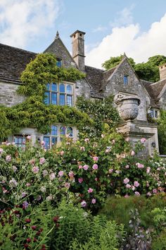 an old stone house surrounded by flowers and greenery