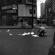 a man kneeling down on the street next to paper airplanes