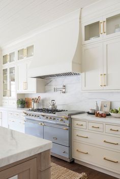 a kitchen with white cabinets and marble counter tops, gold pulls on the oven hood