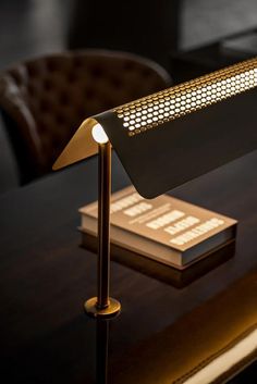 a desk lamp sitting on top of a wooden table next to a brown chair and book