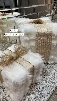 two white fur boxes with gold bows on them sitting on a marble counter in front of a mirror