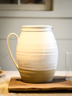 a white vase sitting on top of a wooden cutting board next to a glass cup