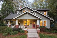 a gray house with red front door and white trim is lit up by the sun