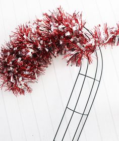 red and white tinsel wrapped branches on a wire stand against a white wall with wood planks in the background