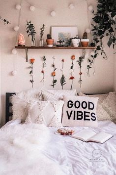 a white bed topped with lots of pillows next to a shelf filled with potted plants