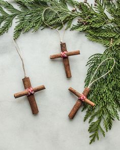 cinnamon stick cross ornament with twine on white surface next to evergreen branches