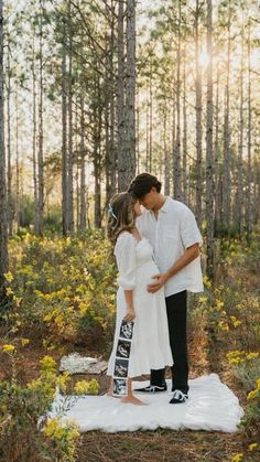 a man and woman kissing in the woods on a blanket with yellow flowers around them