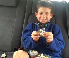 a young boy sitting in the back seat of a car holding a coin and legos