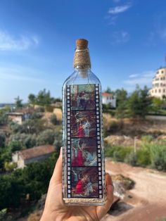 someone holding up a bottle with pictures on it in front of a blue sky and some trees