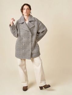 a woman standing in front of a white background wearing a black and white checkered coat