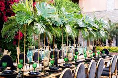 a long table set up with green and black plates, place settings and palm trees