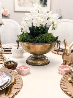 there is a bowl with flowers in it on the dining room table set for two