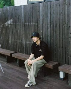 a young man sitting on top of a bench next to a wooden fence and wearing a black hat