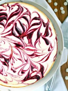 a cheesecake with red and white swirled toppings on a plate next to silverware