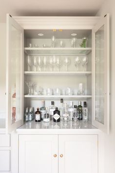 a white cabinet filled with lots of bottles and glasses on top of it's shelves