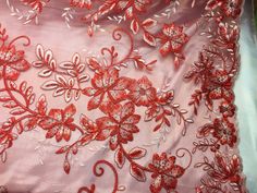 an embroidered fabric with red flowers and leaves on pink silk, showing the delicate lace work