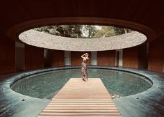 a woman standing on a wooden platform in front of a circular pool with water running through it