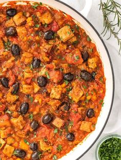 an overhead view of a dish with olives and tofu in tomato sauce, garnished with fresh herbs