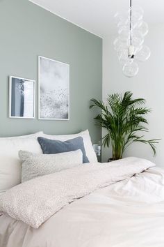 a bed with white sheets and pillows next to a potted plant