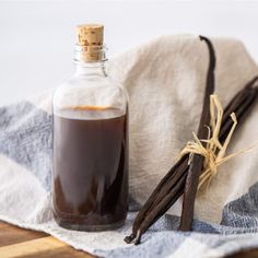 a bottle of vanilla syrup next to cinnamon sticks on a cloth and wooden cutting board