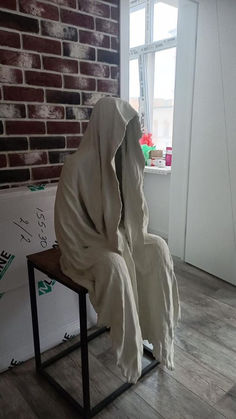 a sculpture is sitting on a chair in front of a brick wall and window, covered with a white cloth