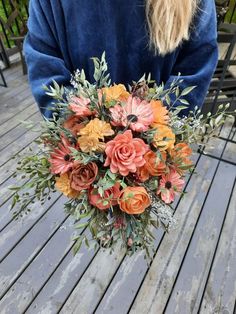 a woman holding a bouquet of flowers on top of a wooden deck