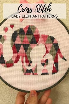 the cross stitch elephant pattern is being held up by someone's hand and has pink bows on it