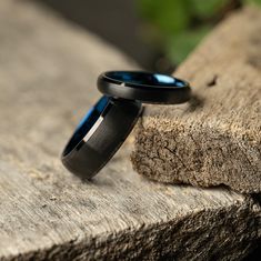 two wedding rings sitting on top of a piece of wood next to each other with blue stone in the background