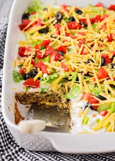 a casserole dish with cheese, black olives, tomatoes and lettuce