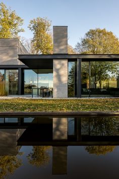 the house is surrounded by trees and has glass walls on both sides, along with its reflection in the water