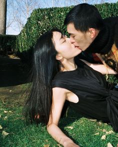 a man and woman kissing in the grass with a dog on their lap next to them