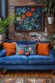 a blue couch with orange pillows in front of a brick wall and potted plants