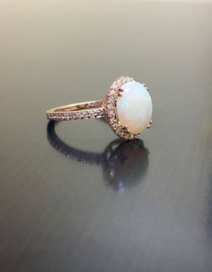 DeKara Designs Collection Our latest design! An elegant and lustrous Opal cabochon surrounded by beautiful diamonds in a halo setting. Metal- 18K Rose Gold, .750. This Specific Ring Is a Size 6 3/4 Stones- Center Features an Oval Fiery Australian Opal Cabochon Cut 2.20 Carats, 11.10 MM Long, 9 MM Wide, 44 Round Diamonds, H-I Color VS2-SI1 Clarity, 0.40 Carats. Latest of my creations. A beautiful Opal Halo Diamond Ring. The Opal is professionally prong set in between 4 double prongs. There are 10 Elegant Round Opal Ring For Formal Occasions, Elegant Round Opal Ring For Formal Events, Elegant Opal Ring With Diamond In Rose Gold, Rose Gold Opal Diamond Ring In Fine Jewelry Style, Rose Gold Diamond Opal Ring Fine Jewelry, Rose Gold Opal Diamond Ring Fine Jewelry, Rose Gold Opal Diamond Ring, Elegant White Gold Opal Ring, Elegant Rose Gold Opal Ring With Diamond