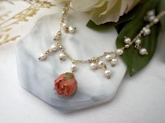 a close up of a necklace on a white surface with flowers in the back ground