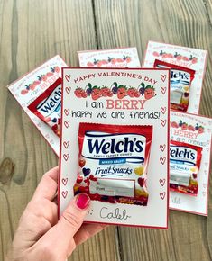 four valentine's day candy packets are shown in front of a wooden table with two hands holding them