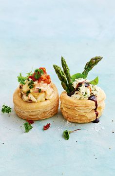 two pastries with asparagus and other toppings on them sitting on a blue surface