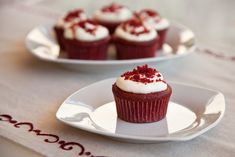 a cupcake with white frosting and red sprinkles sits on a plate