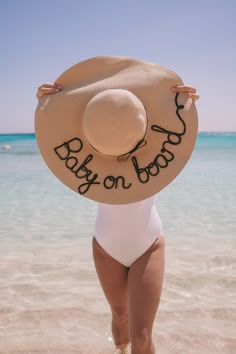 a woman in a white bodysuit and hat standing on the beach with her back to the camera