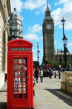 a red phone booth sitting on the side of a street next to a clock tower