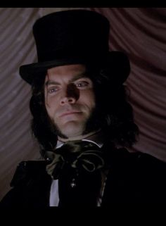 a man with long hair wearing a top hat and bow tie in a dark room