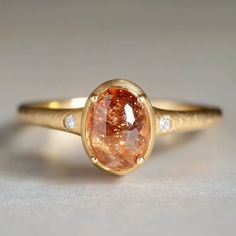 **Capture the warmth of the sun with our beautiful engagement ring, featuring a radiant sunstone at its center and two accent diamonds on either side. *Gem - 6*9.5mm Sunstone, 2mm diamond Finish: Brush finish *Gems: The natural gems natural hues vary, adding an organic touch to your ensemble. I'll try to select them in the spectrum as close to the picture as possible. Want to see your specific stone? Just send me an email, and I'll happily provide photos for you to choose from. *Metal: Delicatel Raw Rings Engagement, Colorful Vintage Engagement Rings, Matte Gold Ring, Engagement Ring Without Diamond, Funky Wedding Ring, Non Engagement Rings, Gold Gemstone Wedding Rings, Engagement Rings With Stones, Vintage Rings Aesthetic